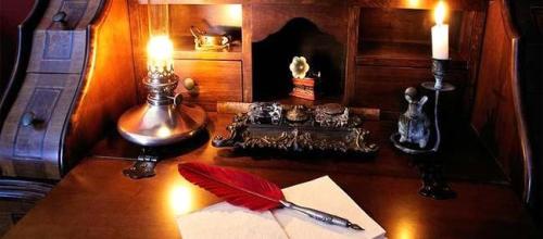 Antique writing desk with red feather quill pen and oil lamp